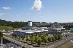 緑豊かな丘陵地を背に、特徴的な円筒形の建物を囲む円形の施設や複数の平屋建ての施設が並ぶ茂庭浄水場の全景を写した写真