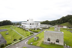 緑豊かな丘陵地に位置し、手前にコンクリート造りの小規模な構造物、奥に白い大きな管理棟が建つ福岡浄水場の全景を写した写真