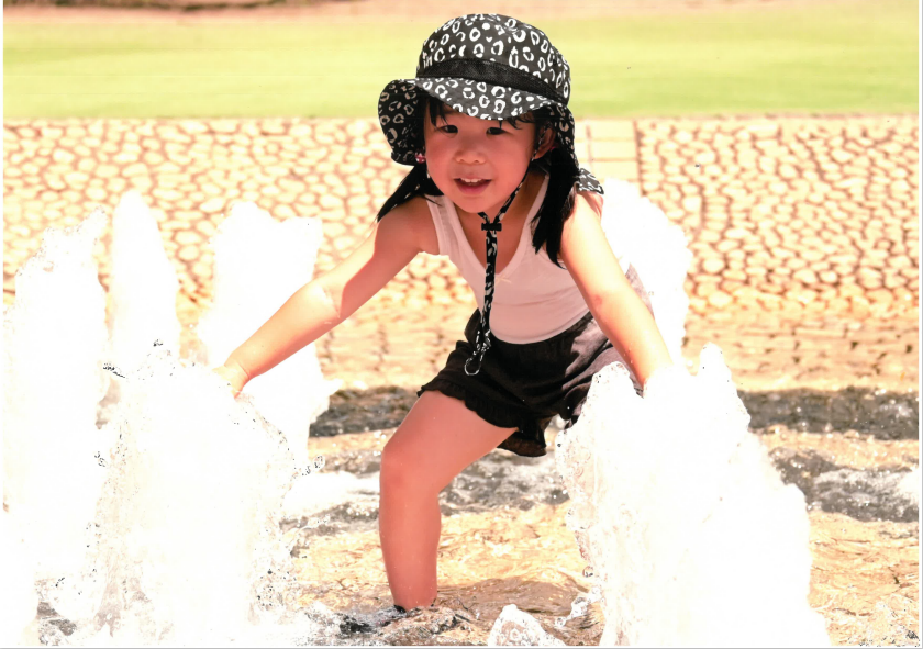 帽子をかぶった少女が噴水で水遊びをする様子の写真