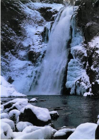 雪化粧の秋湯大滝が水しぶきとともに流れる様子の写真