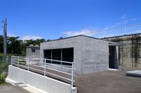手前には白い手すりが付いたコンクリート造平屋建ての安養寺配水所小水力発電設備建屋の外観写真
