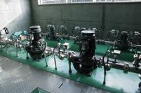 屋内の緑色の床面に、黒色のポンプや小型の機械が、配管とともに一列に並んで設置されている安養寺配水所小水力発電設備の発電機の写真