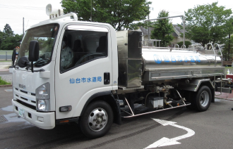 車体に「仙台市水道局」と書かれ、荷台にステンレス製の給水タンクを搭載した給水車が屋外に停車している写真