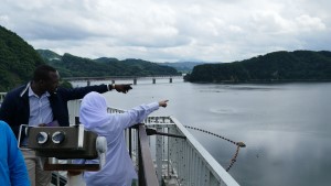 派遣研究員が、展望台のフェンス越しに、広大な釜房ダムや遠方の山々を指差しながら景色を眺めている様子の写真
