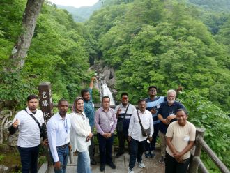 深い緑に包まれた秋保大滝を背景に派遣研究員の方々が並び、少し上から見下ろして撮影した記念写真