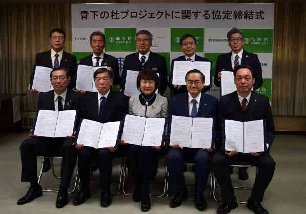 「青下の杜プロジェクトに関する協定締結式」と書かれたパネルの前で、スーツ姿の郡市長と9名の男性が、締結した協定書を手に持ち前後2列に並んでいる記念写真