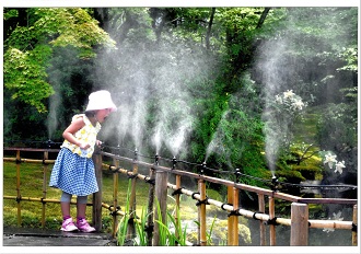 青々とした木々が茂る庭園の竹垣から噴き出すミストを、女の子が楽しそうに浴びている様子の写真