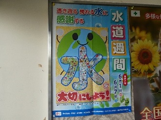 令和7年の水道週間ポスターに、笑顔の地球と多彩なイラストが詰まった「水」の漢字が描かれ、「透き通る 誇れる水に 感謝する 水を大切にしよう！」という標語が書かれているポスターが壁に掲示されている写真