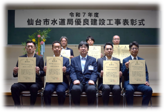 「令和7年度 仙台市水道局優良建設工事表彰式」と書かれた横断幕を背に、賞状を手にしたスーツ姿の受賞者7名が、前列中央に座ったスーツ姿の男性と一緒に、前後2列に並んだ記念写真